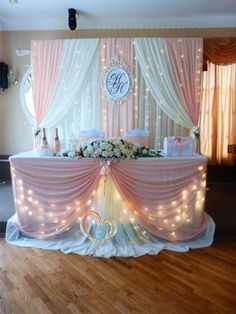 a decorated table with pink and white flowers on it, surrounded by lights in the background