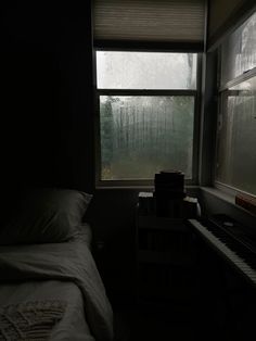 a bed sitting next to a window in a dark room with rain coming through the window