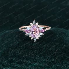 a pink sapphire and diamond ring on a black velvet surface, with the center stone surrounded by diamonds