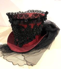 This is elegant Victorian gothic Hand made wine Maroon Top hat with black back beautifully hand crafted feathers and flowers black net bustle train. Top Hat with Black laces and 3D silk flowers and black pearls and dark red jewels and sequins hand stitched.  Please refer to the photos. This is stunning Victorian Steampunk Handmade top hat made with lots of love. It is very well made, this hat is made of a satin type of fabric and the inside of the hat is has a Black satin  lining. The front of t Elegant Red Corset For Costume Party, Fitted Red Halloween Hat, Elegant Halloween Costume Corset, Red Fitted Hat For Costume, Red Fitted Mini Hat For Costume Party, Elegant Halloween Party Corset, Gothic High Crown Hat For Party, Fitted Gothic Hat For Costume Party, Gothic Black Top Hat For Party