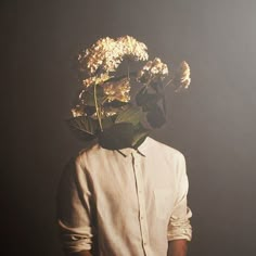 a man standing in front of a black wall with flowers on his head and hands behind him