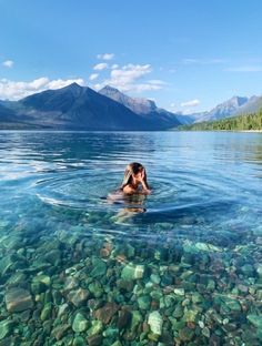 a woman is swimming in the water near mountains