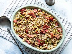 a bowl filled with beans and meat on top of a striped towel next to two spoons