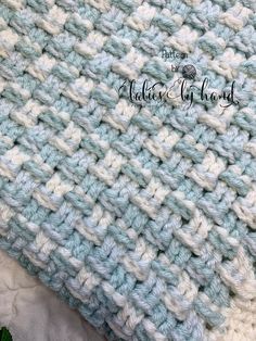 a crocheted blue and white blanket laying on top of a bed