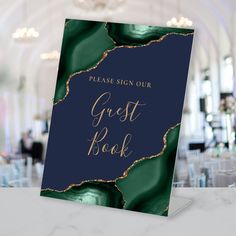 a blue and green guest book with gold foil lettering on the cover, sitting on a marble table