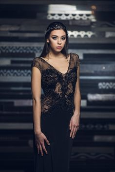 a woman standing in front of a dark background wearing a black dress and headpiece