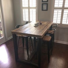 a wooden table sitting in the middle of a living room next to two bar stools