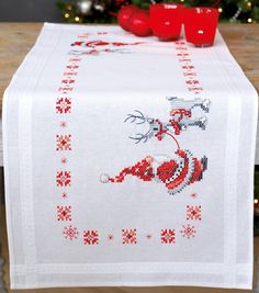 a christmas table runner with red cups on it and a small tree in the background