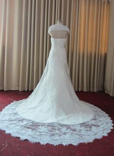 a wedding dress is displayed on a mannequin in front of curtained windows