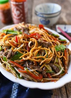 a white plate filled with noodles and meat on top of a table next to chopsticks