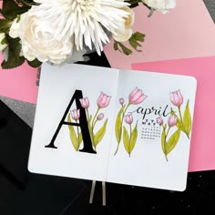 an open notebook sitting on top of a table next to a vase with white flowers