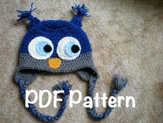 a crocheted blue and gray hat with an owl face on the front, sitting on top of a carpet