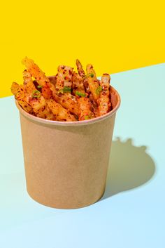 a paper cup filled with fried food on top of a white table next to a yellow wall