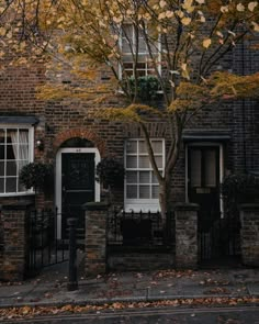 an old brick building with black doors and windows on the front, surrounded by autumn leaves