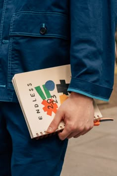 a person holding a notebook and pen in their hand while standing on the sidewalk outside