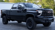 a black truck parked in a parking lot next to a white building with trees behind it