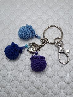 three crocheted keychains are sitting on a white surface, one is blue and the other is purple