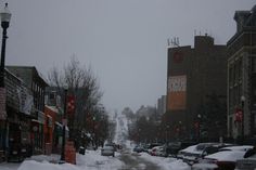 a snowy street with cars parked on both sides and buildings in the background, all covered by snow