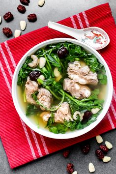 a white bowl filled with meat and greens on top of a red napkin next to nuts