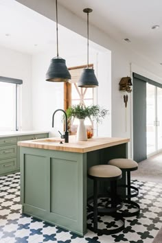 a kitchen with green cabinets and black pendant lights hanging over the island in front of two stools