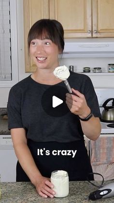 a woman standing in front of a kitchen counter holding a spoon with whipped cream on it