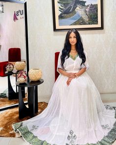 a woman sitting on a chair in front of a mirror wearing a long white dress