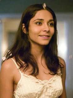 a woman with long dark hair wearing a white top and smiling at the camera while standing in front of a mirror