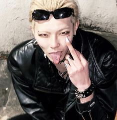 a young man with his tongue out and sunglasses on, making a silly face while sitting down