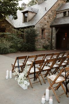 a row of wooden folding chairs with white flowers and candles on the ground in front of a stone building