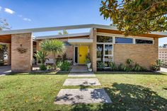 a house with a yellow door and some plants in the front yard on a sunny day