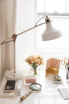 a white desk topped with a lamp next to a vase filled with flowers and books