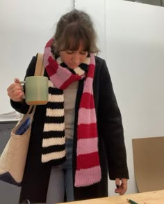 a woman holding a coffee cup and wearing a striped scarf