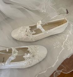 two pairs of white wedding shoes with lace and flowers on the bottom, sitting on a bed