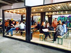 a group of people sitting at tables in front of a building with graffiti on the walls