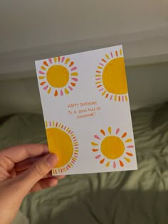 someone is holding up a birthday card with the sun design on it in front of a bed