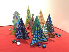 several brightly colored paper christmas trees on a red surface with balls and beads around them