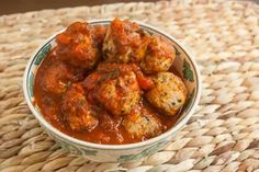 a bowl filled with meatballs covered in sauce on top of a woven place mat