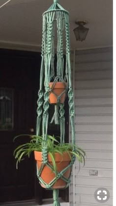 two potted plants are hanging from a green macrame planter on the front porch