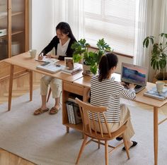 two women sitting at a table with books and laptops on it, one woman is reading