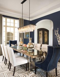 an elegant dining room with blue walls and white chairs, gold chandelier over the table