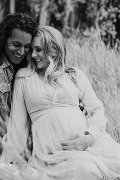 a pregnant couple cuddle together in the grass