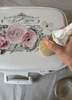 a person holding a paint brush next to a white box with pink flowers on it