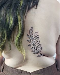 the back of a woman's shoulder with a leaf tattoo on it