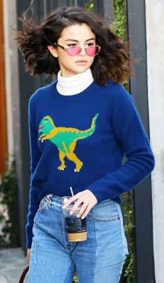 a woman in blue sweater and jeans walking down the street