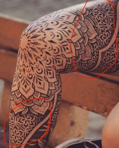 a woman's leg with an intricate tattoo design on her arm and leg, in front of a wooden bench