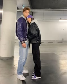 two people standing next to each other in an empty parking garage with one person wearing a leather jacket