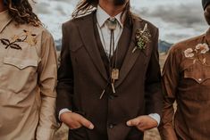 three men standing next to each other with long hair and beards wearing brown suits