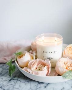 a white candle sitting on top of a plate filled with flowers