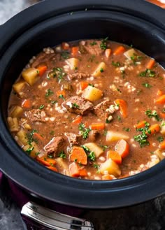 a crock pot filled with beef stew and carrots on top of a table