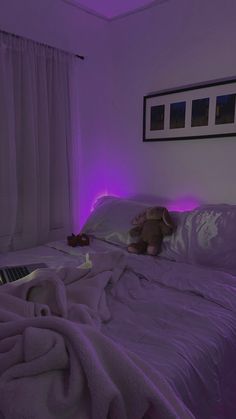 a teddy bear sitting on top of a bed in a room with purple light coming from the ceiling